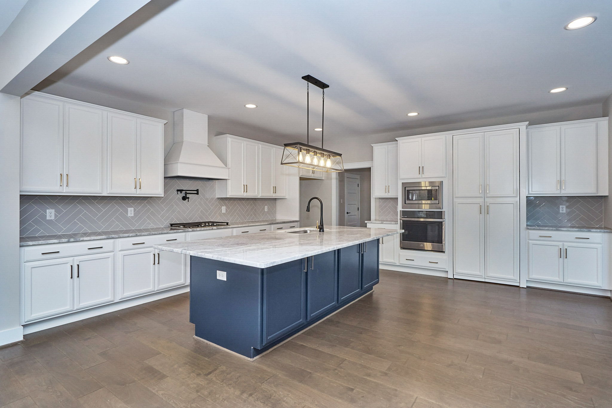 Modern kitchen with white cabinets, blue island, stainless steel appliances, and pendant lighting.