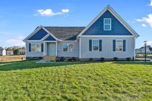 New single-story house with grey siding and blue shutters, well-manicured front lawn under a clear blue sky.