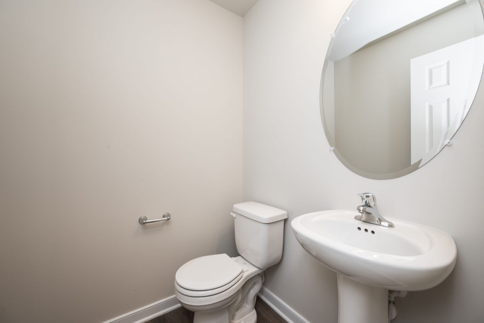 Minimalist bathroom with a white toilet, pedestal sink, and round mirror on light-colored walls.