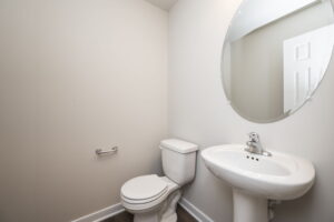 Minimalist bathroom with a white toilet, pedestal sink, and round mirror on light-colored walls.