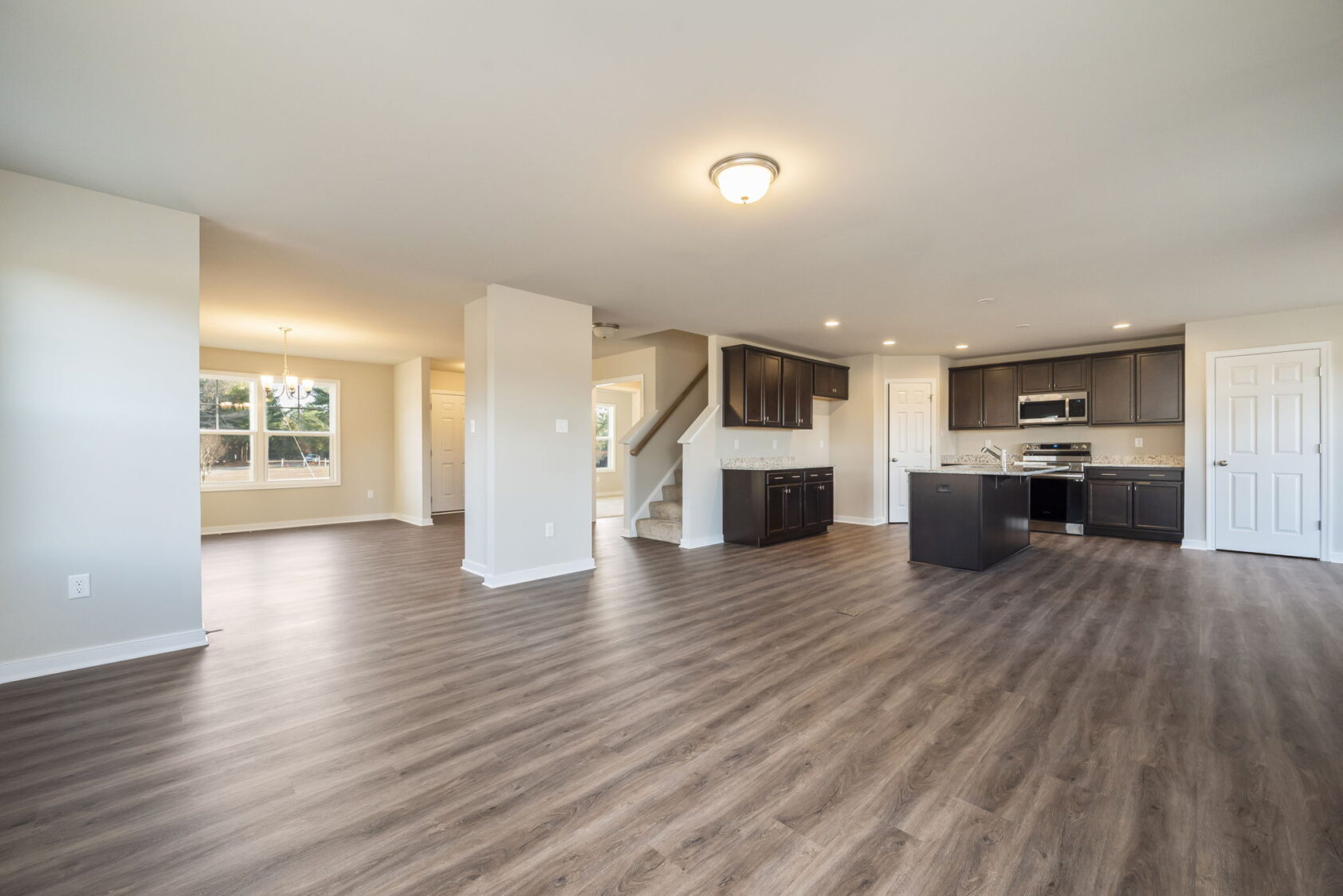 Open-concept living area with wood floors, modern kitchen, and staircase leading to an upper floor.