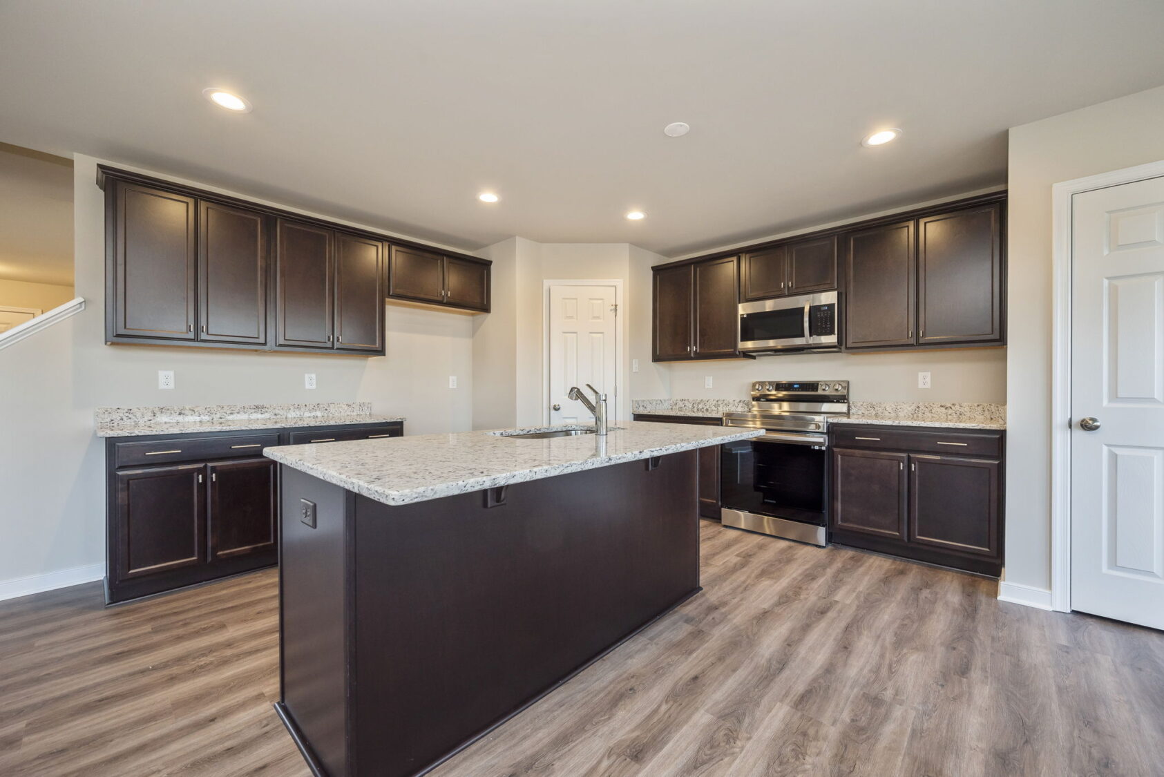 Modern kitchen with dark cabinets, granite countertops, stainless steel appliances, and a center island.