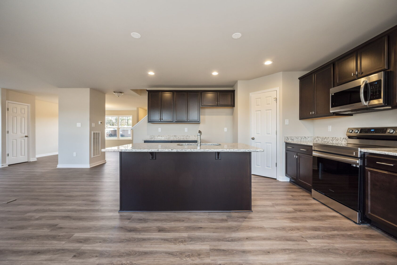 Modern kitchen with dark cabinets, granite countertops, island, and stainless steel appliances, open to living area.
