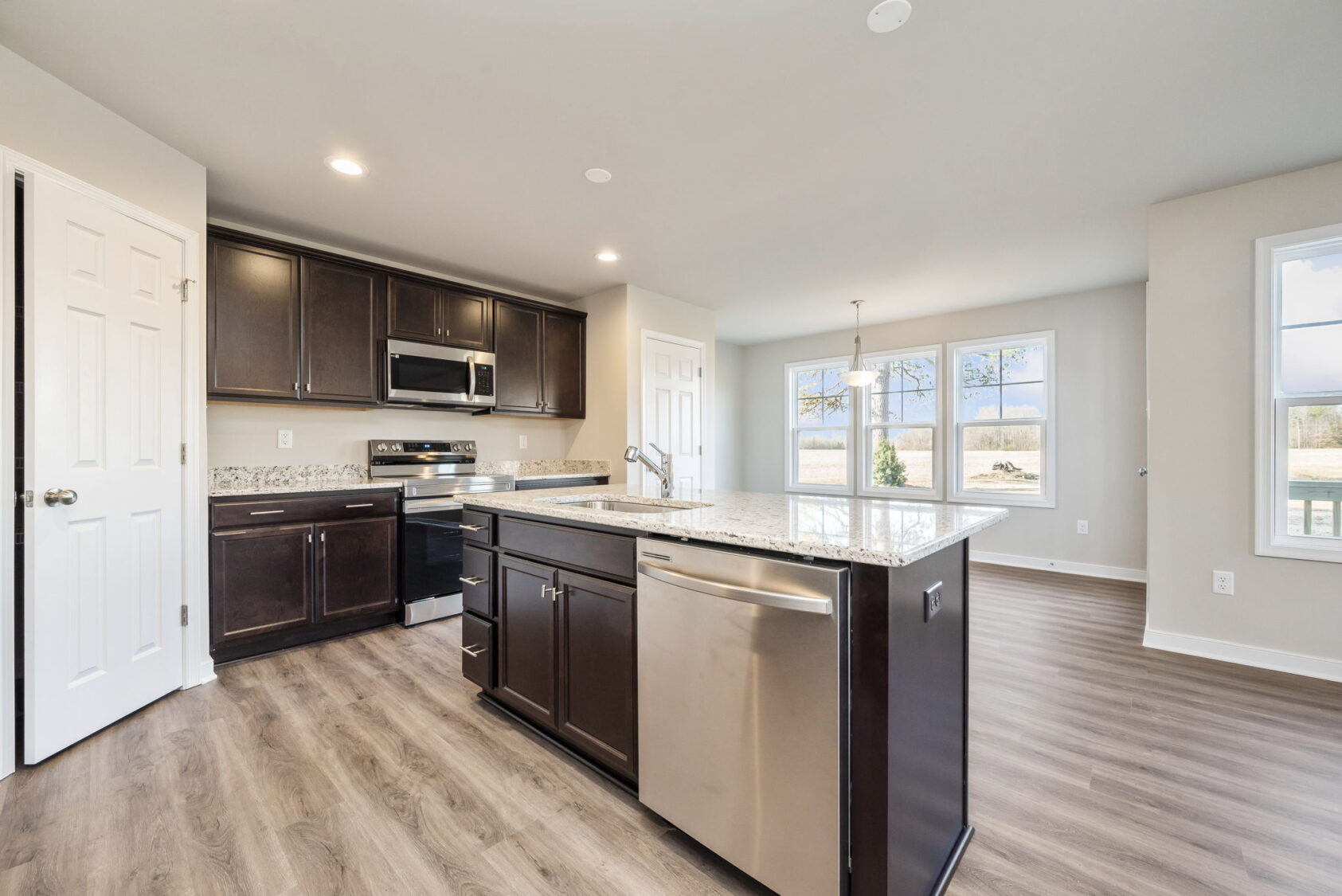 Modern kitchen with dark cabinets, granite countertops, stainless steel appliances, and wood-style flooring.