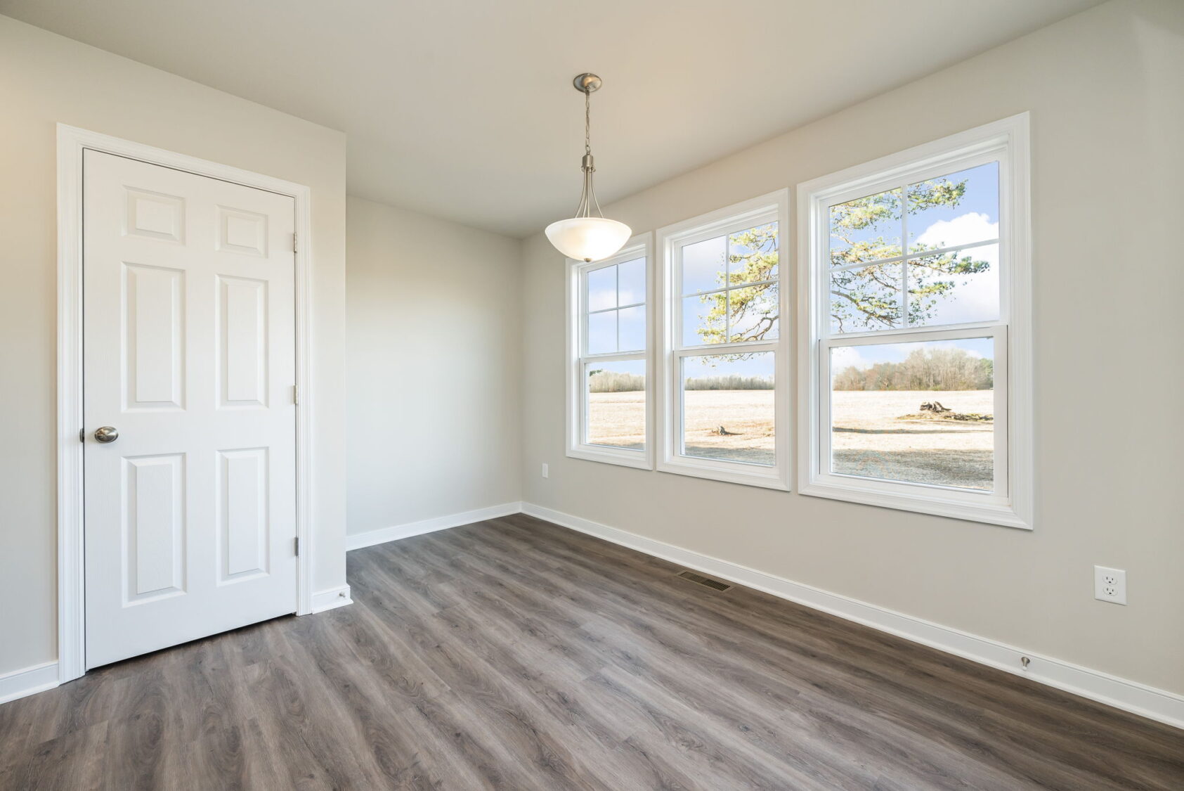 Bright room with large windows, wood flooring, a white door, and a hanging light fixture.