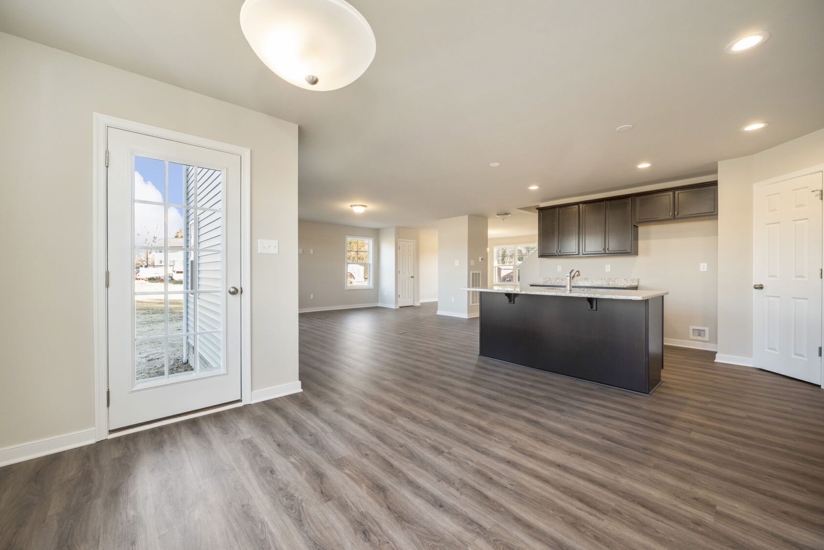 Modern open-plan kitchen and living area with wood flooring, white walls, and large windows for natural light.