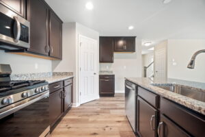Modern kitchen interior with dark wood cabinets, stainless steel appliances, granite countertops, and hardwood floors.