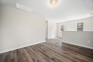 Empty living room with beige walls, wood flooring, and ceiling lights.