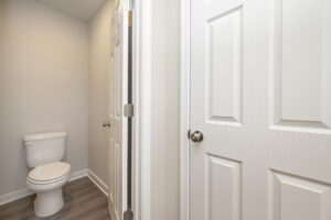 Small bathroom with a white toilet, gray walls, and two closed white doors with silver handles.