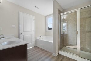 Modern bathroom with a dual sink vanity, large mirror, glass shower stall, and a separate bathtub, featuring beige tiles and white walls.