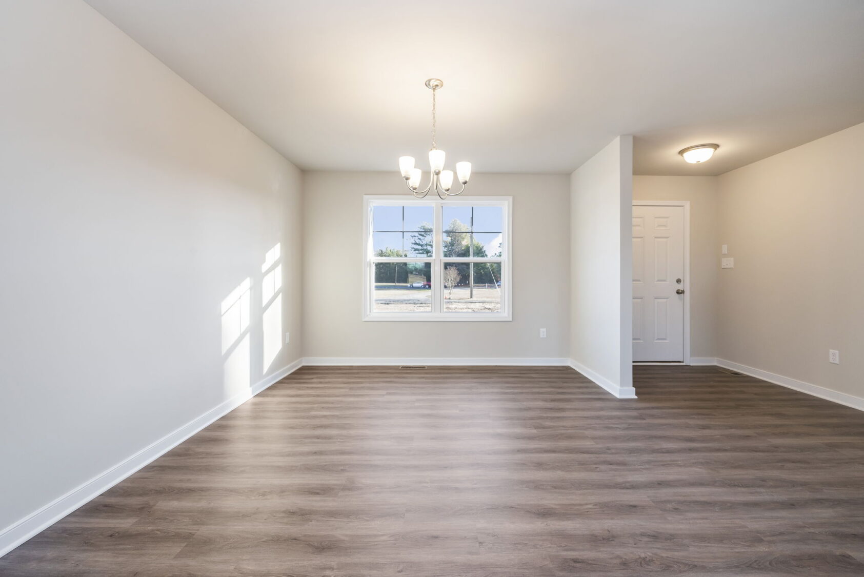 Empty room with light walls, wood flooring, a window, chandelier, and a white door at the back.