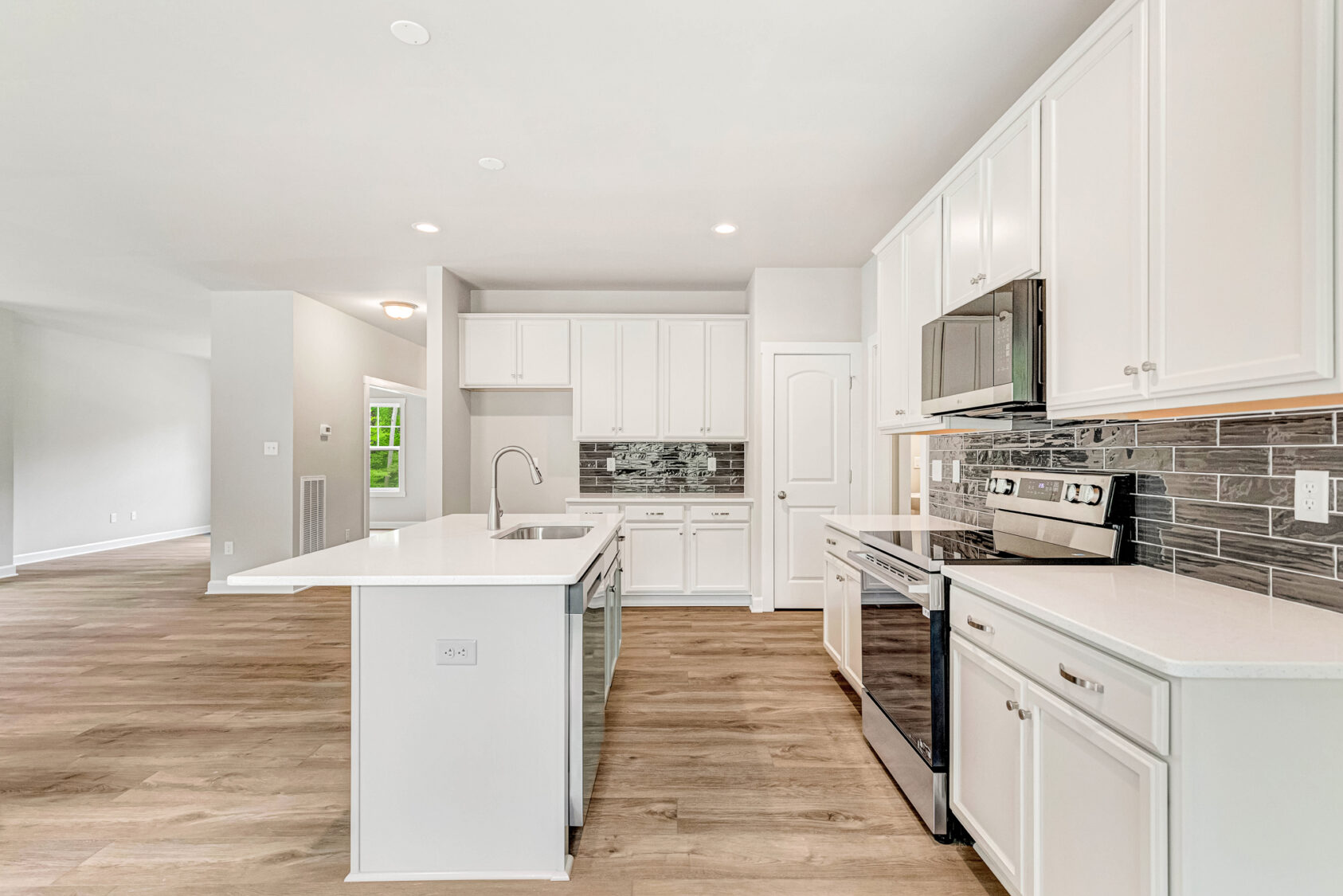 Modern kitchen with white cabinets, stainless steel appliances, and a large island on light wood flooring.