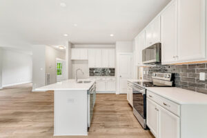 Modern kitchen with white cabinets, stainless steel appliances, and a large island on light wood flooring.