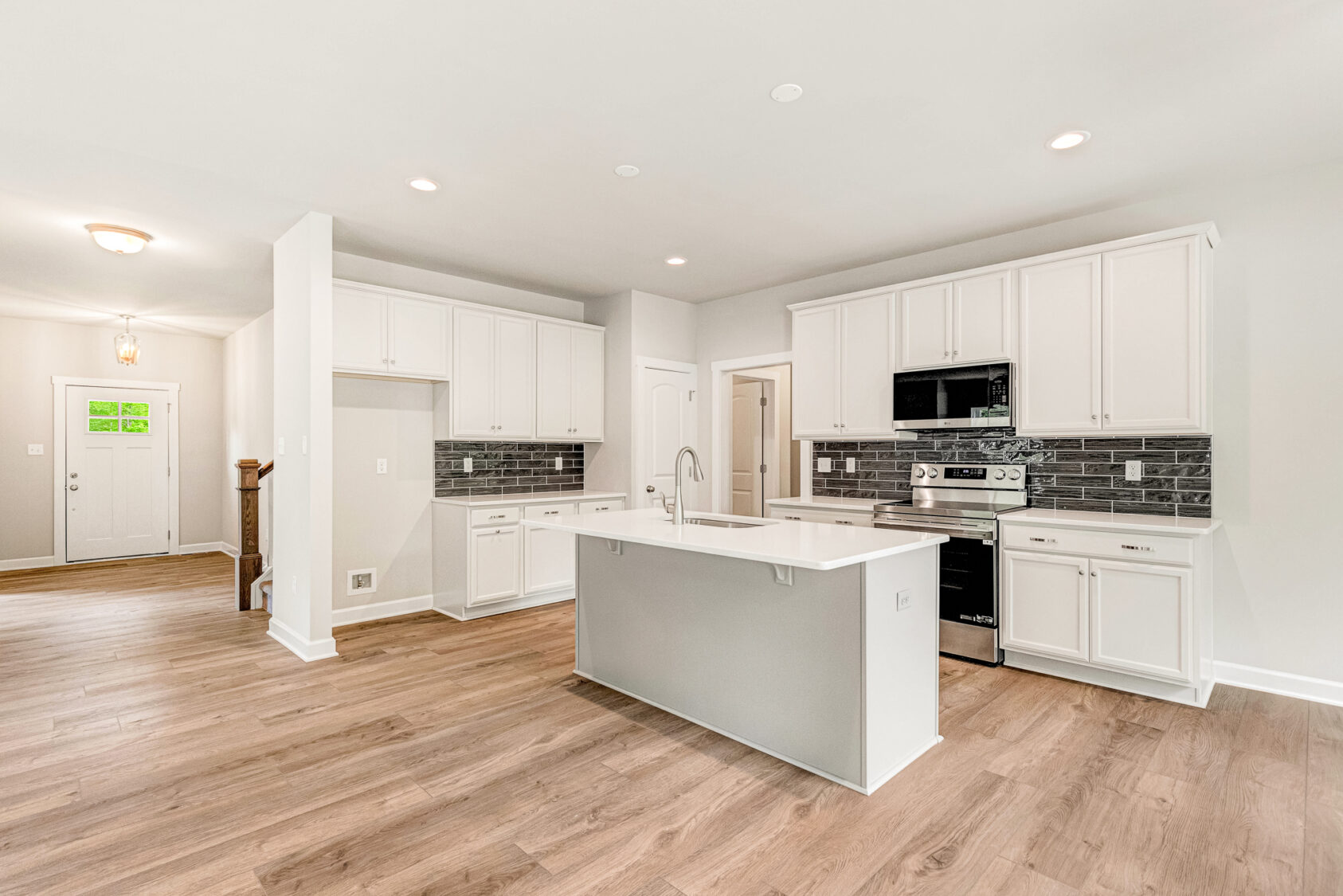 Bright modern kitchen with white cabinets, island, black tile backsplash, and wood flooring.