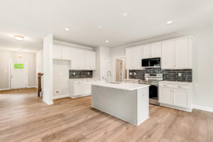 Bright modern kitchen with white cabinets, island, black tile backsplash, and wood flooring.