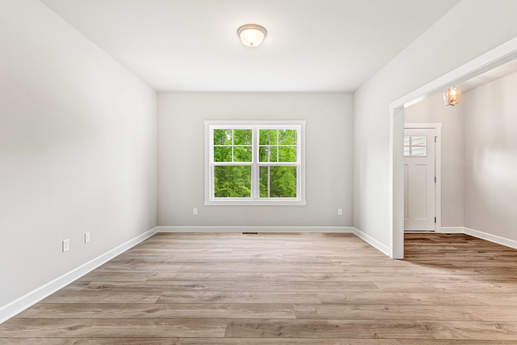 Empty room with light wood floors, white walls, a window, and an open doorway to an entryway.