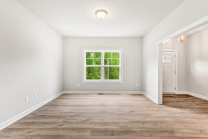 Empty room with light wood floors, white walls, a window, and an open doorway to an entryway.