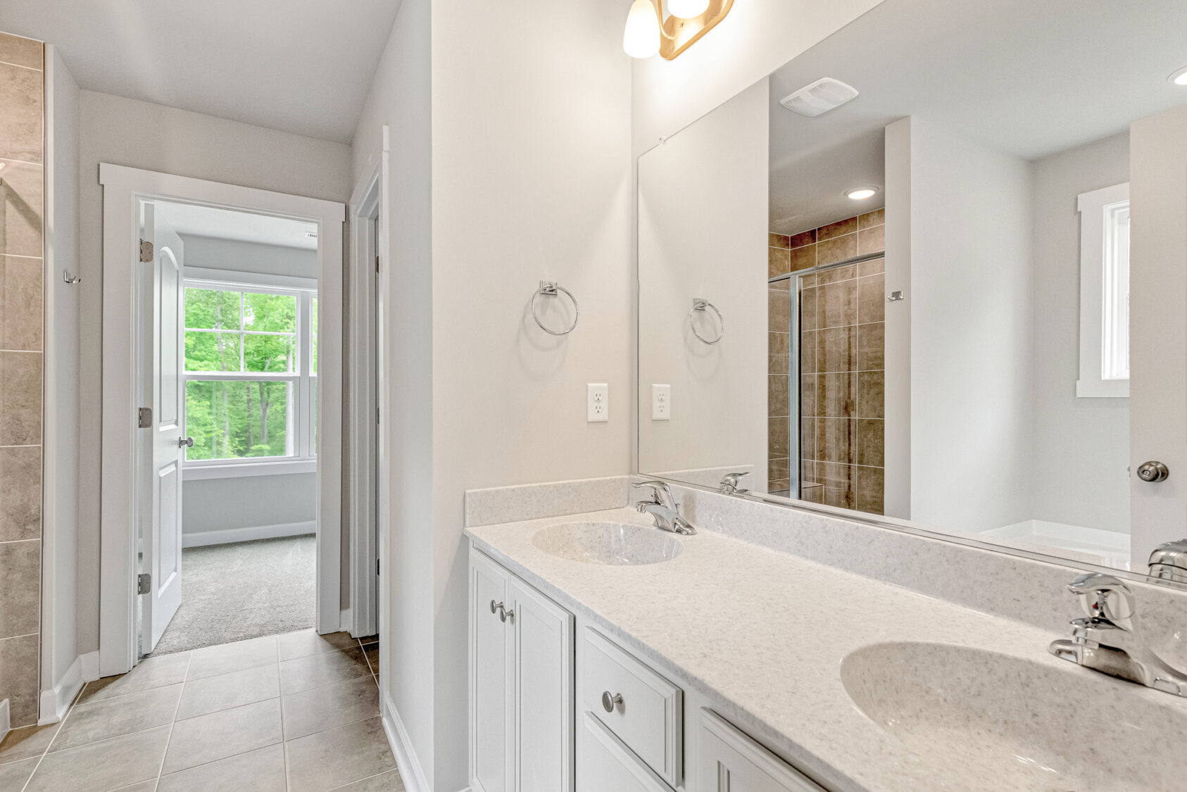 Modern bathroom with double sinks, large mirror, tiled shower, and view into a bright bedroom with large window.