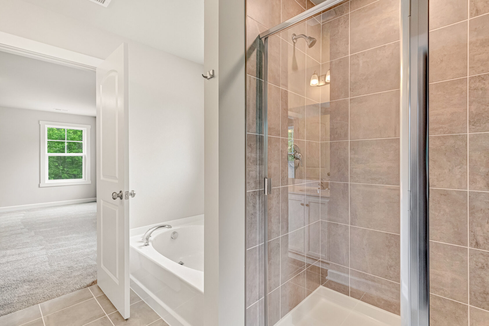 Modern bathroom with glass shower, built-in tub, gray tiles, and view into a bright carpeted bedroom with window.