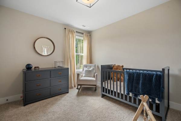 Haley Meadows' minimalist nursery features a crib, chair, dresser, and round mirror. Soft lighting and neutral tones create a cozy atmosphere.
