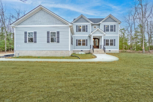 This large gray Manchester house features elegant white trim, black shutters, and a welcoming front porch. It's beautifully situated amidst a spacious grassy yard, offering both charm and serenity.