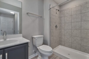 A bathroom with a toilet, sink, mirror, and a walk-in shower with beige tiles and a glass door.