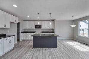 Modern kitchen with white cabinets, black countertops, island with sink, pendant lights, and adjacent dining area. A window provides natural light.