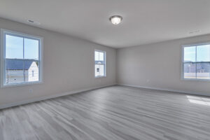 Spacious empty room with light gray wood flooring and white walls, featuring three large windows and a ceiling light fixture.