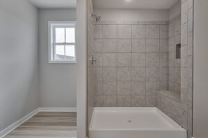 A tiled shower with a built-in bench and niche, adjacent to a window and wood-like flooring.