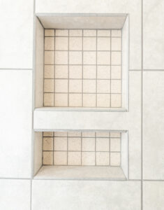 Two recessed shelves with small square tiles are built into a white tiled wall.