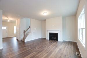 Spacious living room with hardwood floor, fireplace, and large window in Lot 31, Poplar Village. Staircase near front door visible.