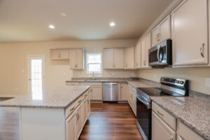 Modern kitchen in Poplar Village with light cabinets, granite countertops, stainless steel appliances, and wood flooring.