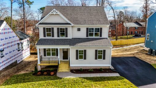 This charming two-story white house on Lot 31 in Poplar Village features a front porch, driveway, and serene tree surroundings.