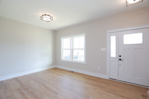 Empty room in Lot 1 with light wood flooring, white walls, a large window, and a white front door with glass panels.