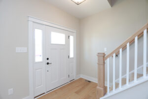 Minimalist entryway in Poplar Village with a white door, wooden floors, and a staircase with white railings.