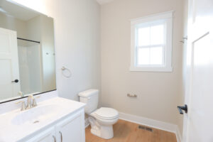 A bright, modern bathroom at Lot 1, Poplar Village features a sink, mirror, toilet, and light wood flooring.