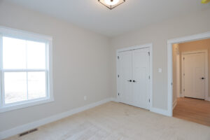 Empty room with beige carpet, white walls, and a window in Poplar Village. Double doors and a doorway lead to another room.