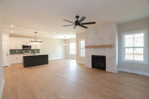 Open-concept living in Poplar Village, Lot 1: light wood flooring, modern kitchen, ceiling fan, and brick fireplace.