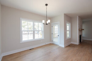 Bright, empty room in Poplar Village with hardwood floor, large window, glass door, and a modern chandelier.