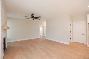 Minimalist living room in Poplar Village: light wood flooring, ceiling fan, brick fireplace, and neutral walls.