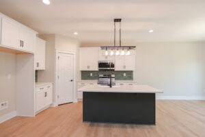 Modern kitchen in Poplar Village with an island, white cabinets, green backsplash, pendant lighting, and light wood flooring.