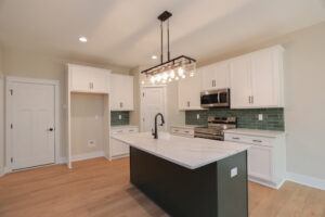 Located in Poplar Village, this modern kitchen features white cabinets, a green tile backsplash, and a center island.