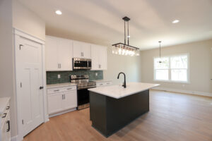 Modern kitchen in Poplar Village, Lot 1, featuring white cabinets, green backsplash, and an island with pendant lighting.