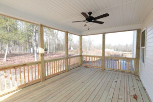 A wooden screened-in porch with a ceiling fan, overlooking Poplar Villages wooded area and serene pond on Lot 1.