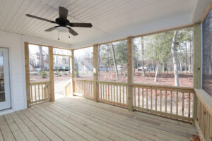 A wooden screened porch with a ceiling fan, overlooking Poplar Villages Lot 1 and trees.