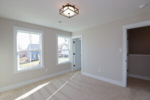 Empty room in Poplar Village with beige walls, carpeted floor, large windows, and modern ceiling light. Door to closet.