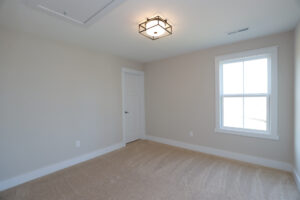 Empty room in Poplar Village with beige walls, carpet flooring, a white door, and a large window letting in natural light.