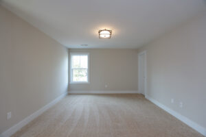 Empty beige carpeted room in Poplar Village with a window, closed door, and modern light fixture on the ceiling.