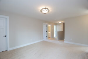 Spacious, empty room in Poplar Village with beige carpet, white walls, two ceiling lights, and open doors to Lot 1.