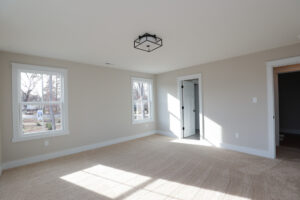 Sunlight streams through the two windows of this Poplar Village, Lot 1 room, featuring beige carpet and pristine white walls.